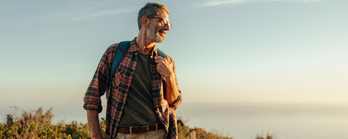 An active older man looks into the setting sun after a day of hiking