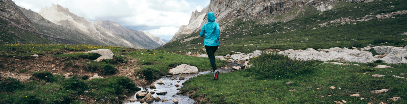 Runner in a brightly colored rain jacket jogging through a lush mountainscape
