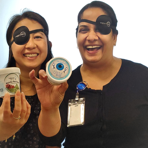 Two people smiling, wearing Castle Cares black eyepatches, and holding Castle Biosciences swag