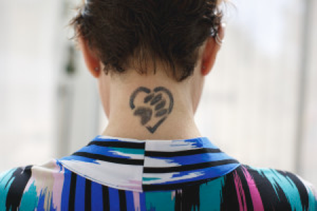 Mary F. displays one of her commemorative remission tattoos on the back of her neck of a dog's paw print in a heart