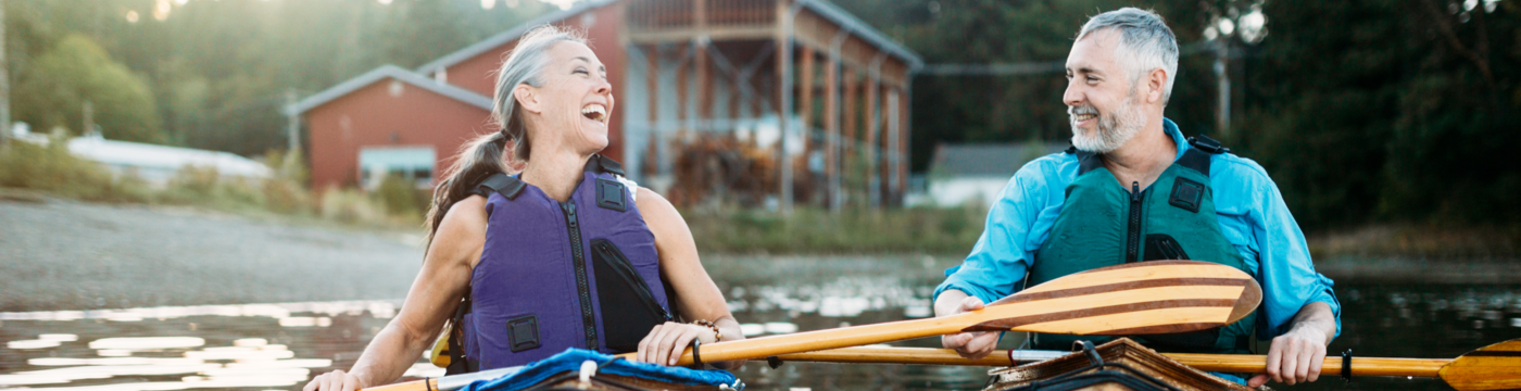 An older couple laugh together while kayaking side by side