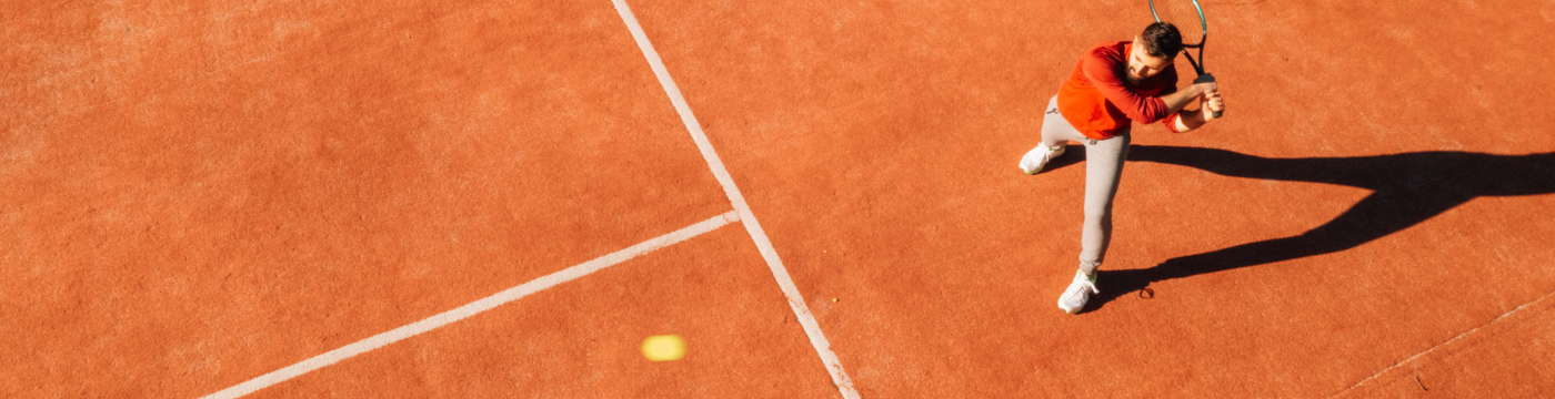 Man on an orange tennis court hitting a tennis ball