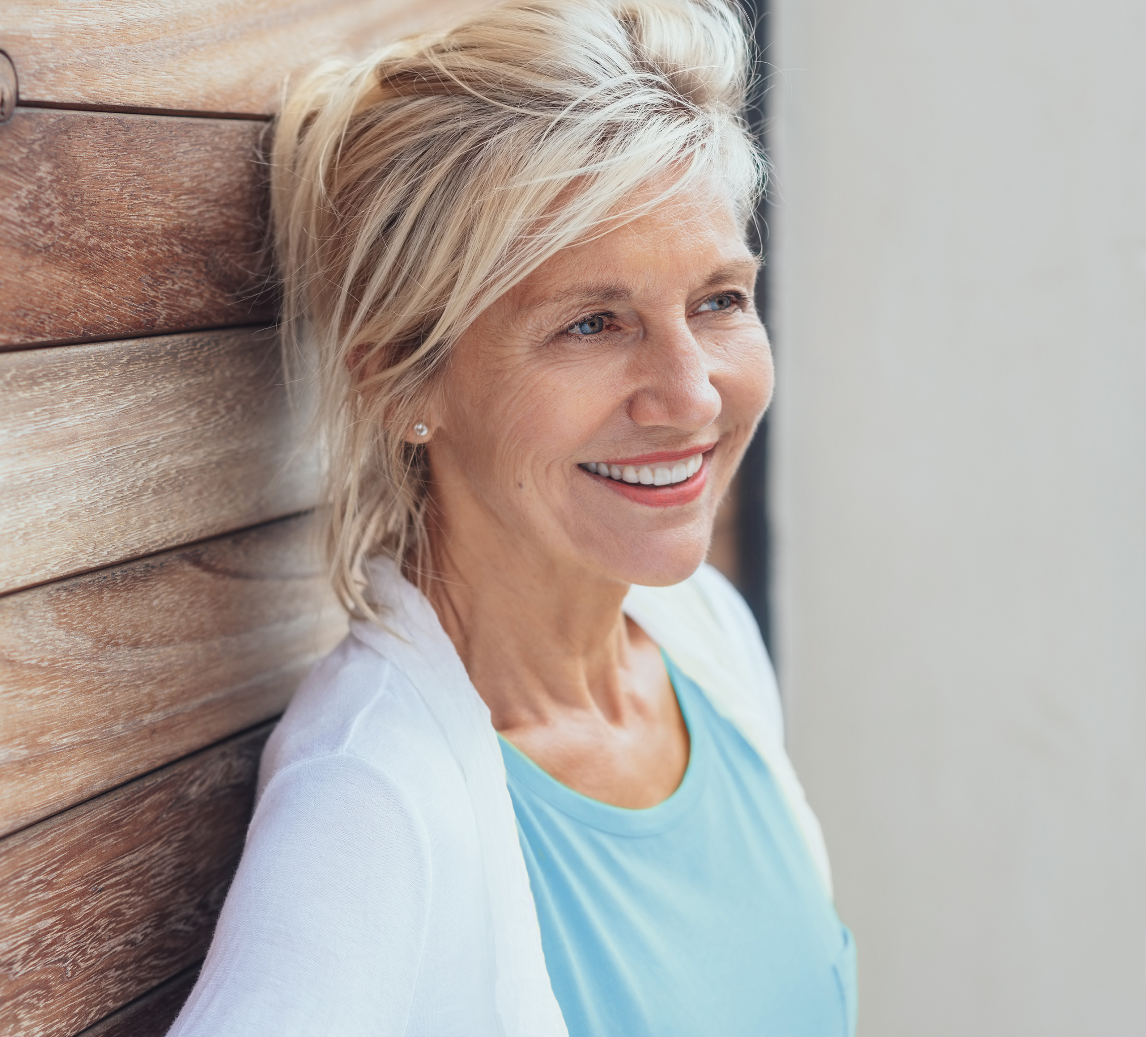 A smiling older woman leans against a wall