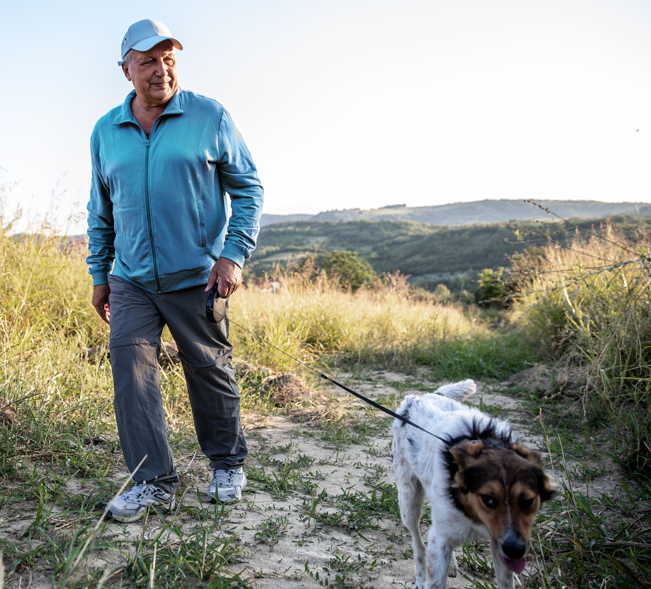 An older man walks his dog on a trail